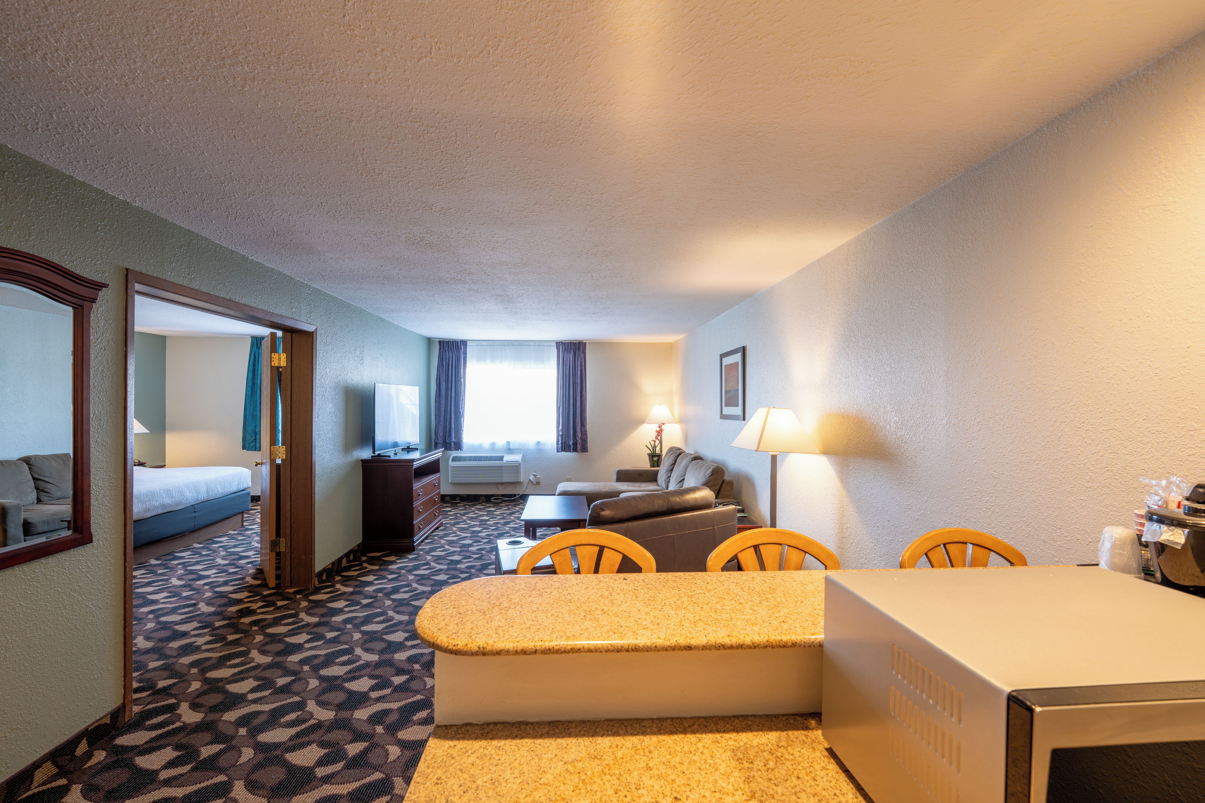A hotel room with a bed, a desk, a chair, a sofa, and a window with curtains.