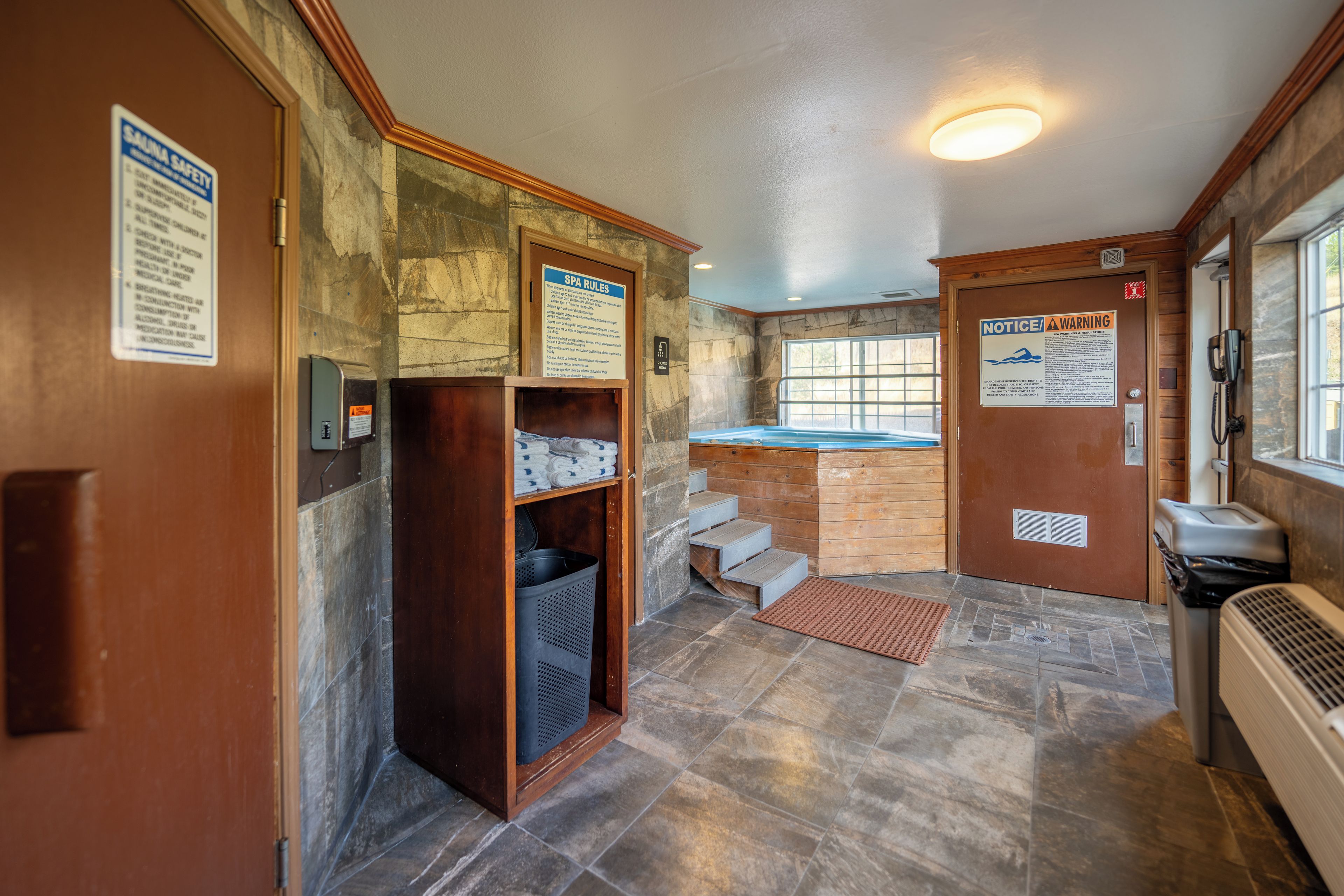 Un cuarto de spa con puerta de madera, un perchero, zona de ducha y un cartel con las normas del spa.