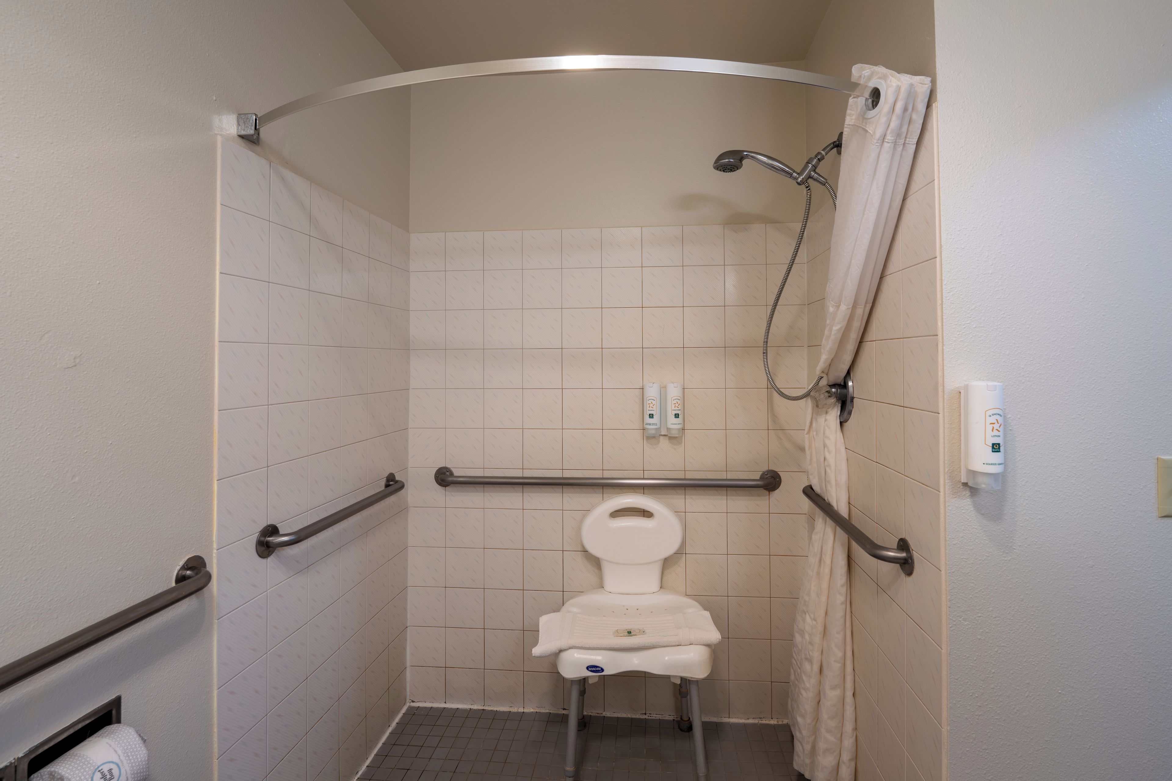 A small, enclosed shower stall with a toilet, grab bars, and a showerhead.