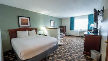 A hotel room with a bed, a desk, a chair, a waste bin, and a window with curtains.