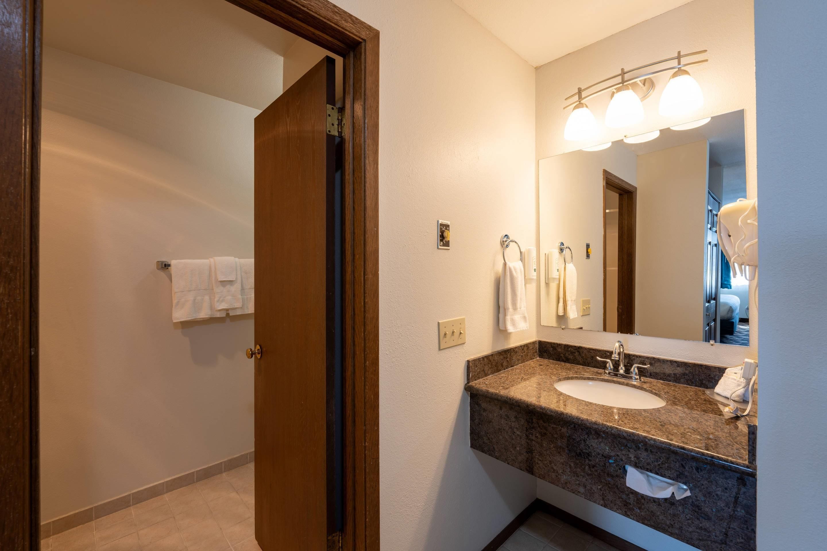 A hotel bathroom with a sink, mirror, towel rack, and a door leading to another room.