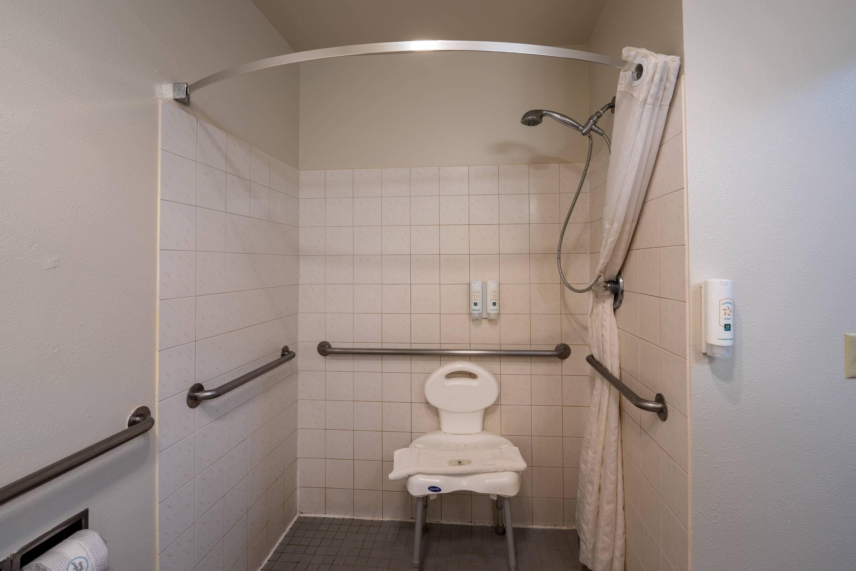 A small, enclosed shower stall with a toilet, grab bars, and a showerhead.
