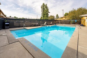 A rectangular swimming pool with a clear blue water surface, surrounded by a black metal fence.
