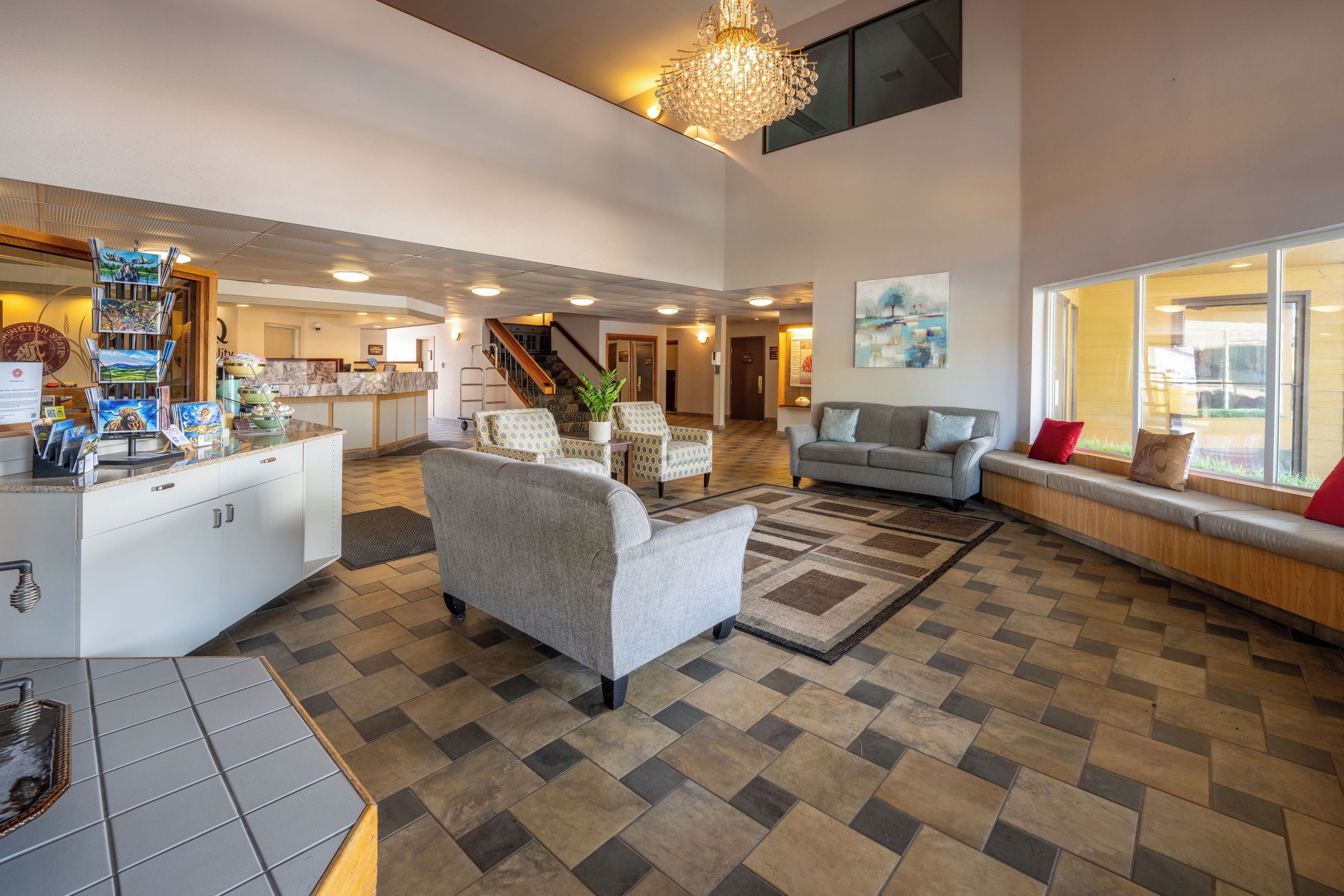 A spacious living area with a high ceiling, a chandelier, and a view of the outdoors through large windows.