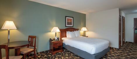 A hotel room with a bed, two bedside lamps, a desk with a chair, and a patterned carpet.