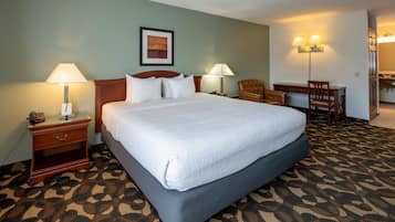 A hotel room with a large bed, two bedside tables with lamps, a chair, a desk, and a painting on the wall.