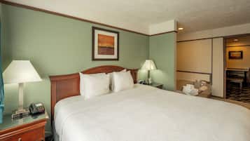 A hotel room with a large bed, two bedside tables with lamps, a painting on the wall, and a bathroom visible through an open door.