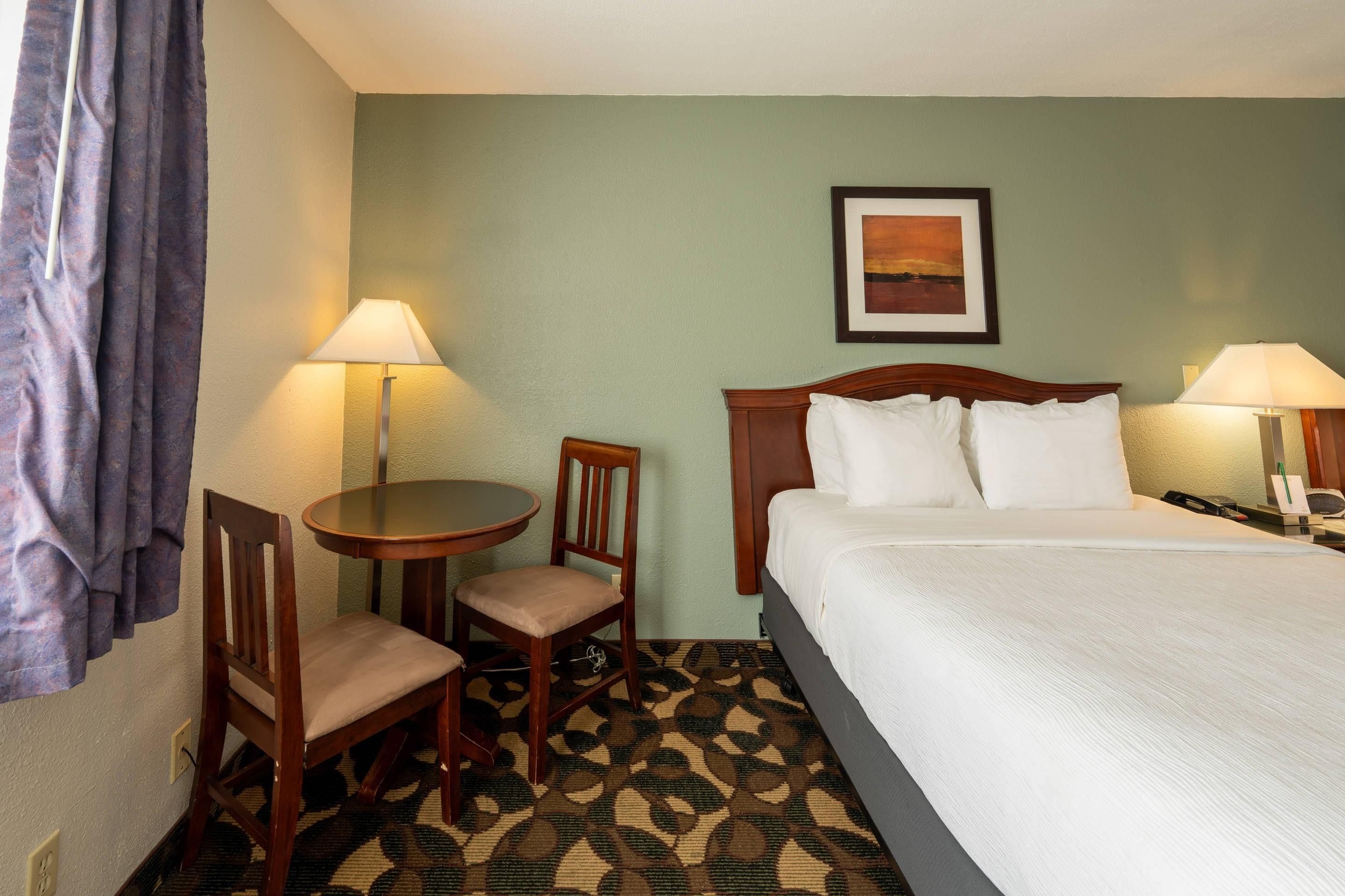 Una habitación de hotel con una cama, dos sillas, una mesita y dos lámparas.