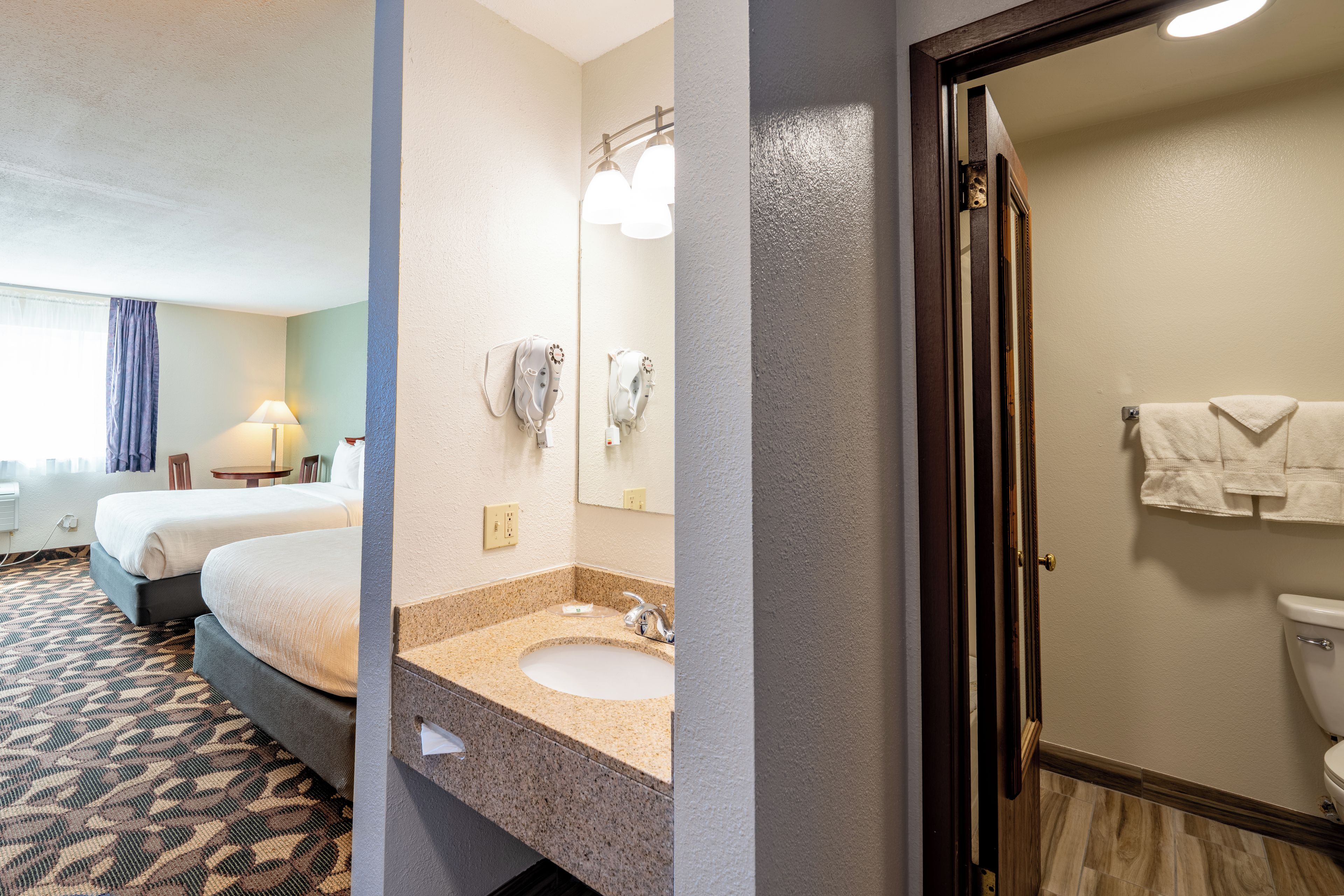 A hotel room with a bed, a bathroom with a sink and mirror, and a toilet.