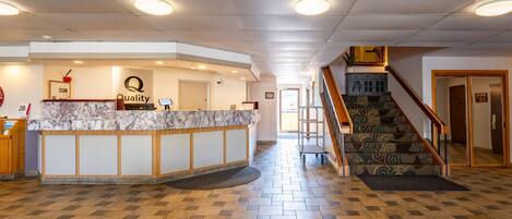 A hotel reception area with a marble counter, a staircase, and a herringbone-patterned floor.