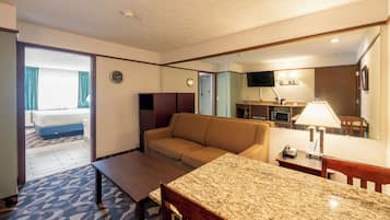 Ein Hotelzimmer mit Sofa, Esstisch, Mikrowelle, Fernseher und einem durch die Tür einsehbarer Badezimmer.