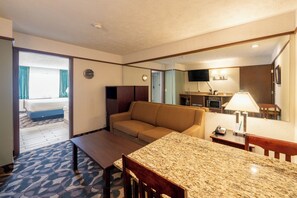 Habitación de hotel con sofá, mesa de comedor, microondas, televisión y baño visible a través de la puerta.
