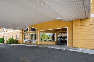 Un hotel con entrada techada, ventanas amplias y un banco en el exterior.