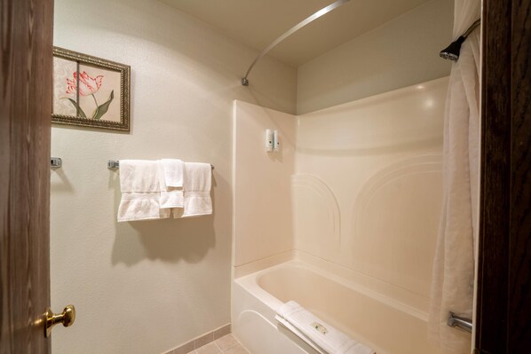 Un baño con bañera, un perchero con dos toallas, un cuadro enmarcado en la pared y una cortina de ducha.