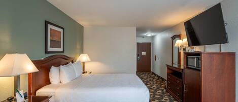 Habitación de hotel con cama, lámparas de noche, televisor, escritorio con teléfono y alfombra estampada.