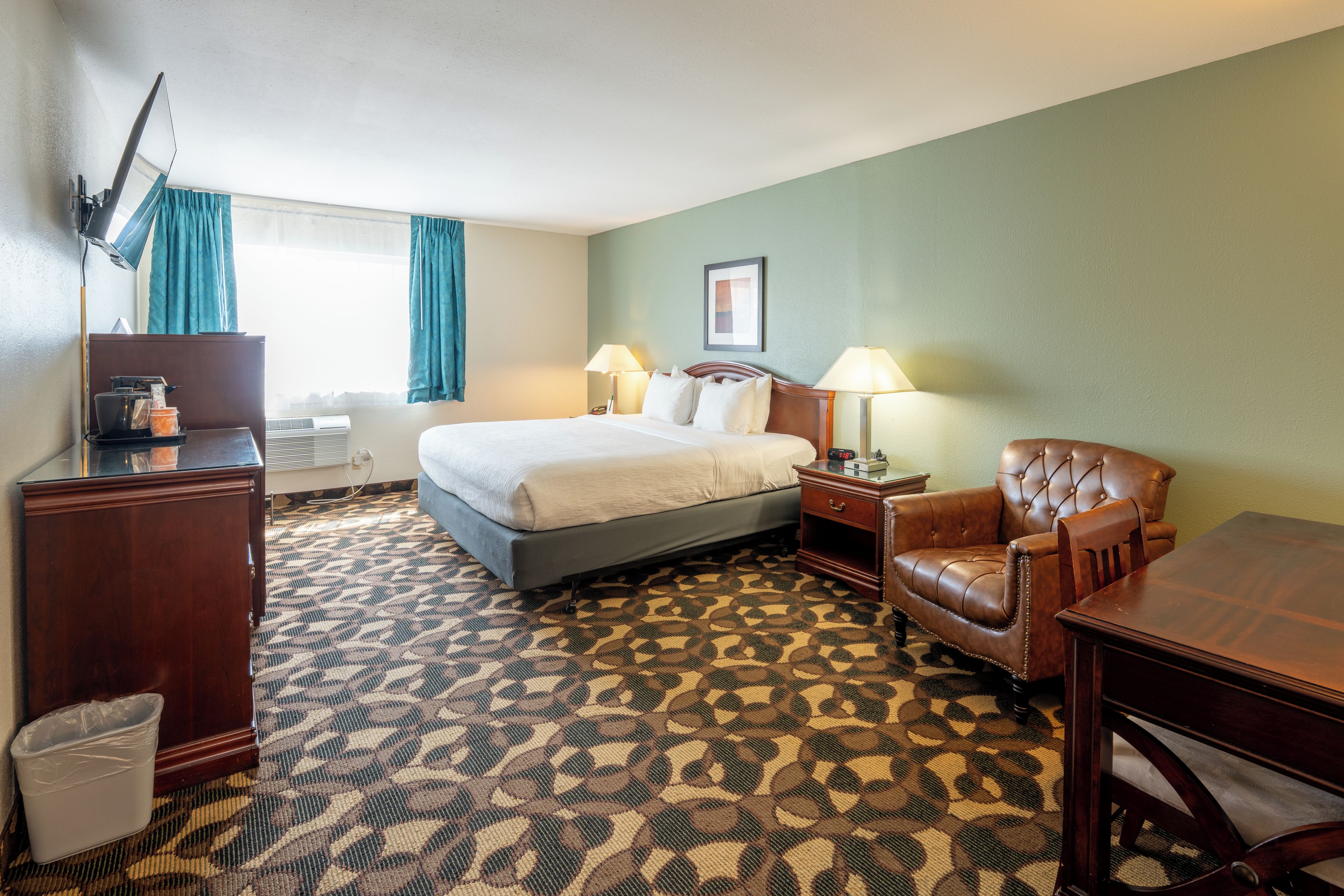 A hotel room with a bed, a desk, a chair, a TV, and a window with curtains.