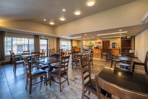 A spacious dining area with multiple tables and chairs, an exit sign, and a kitchen area in the background. - Quality Inn Paradise Creek Pullman (Pullman)