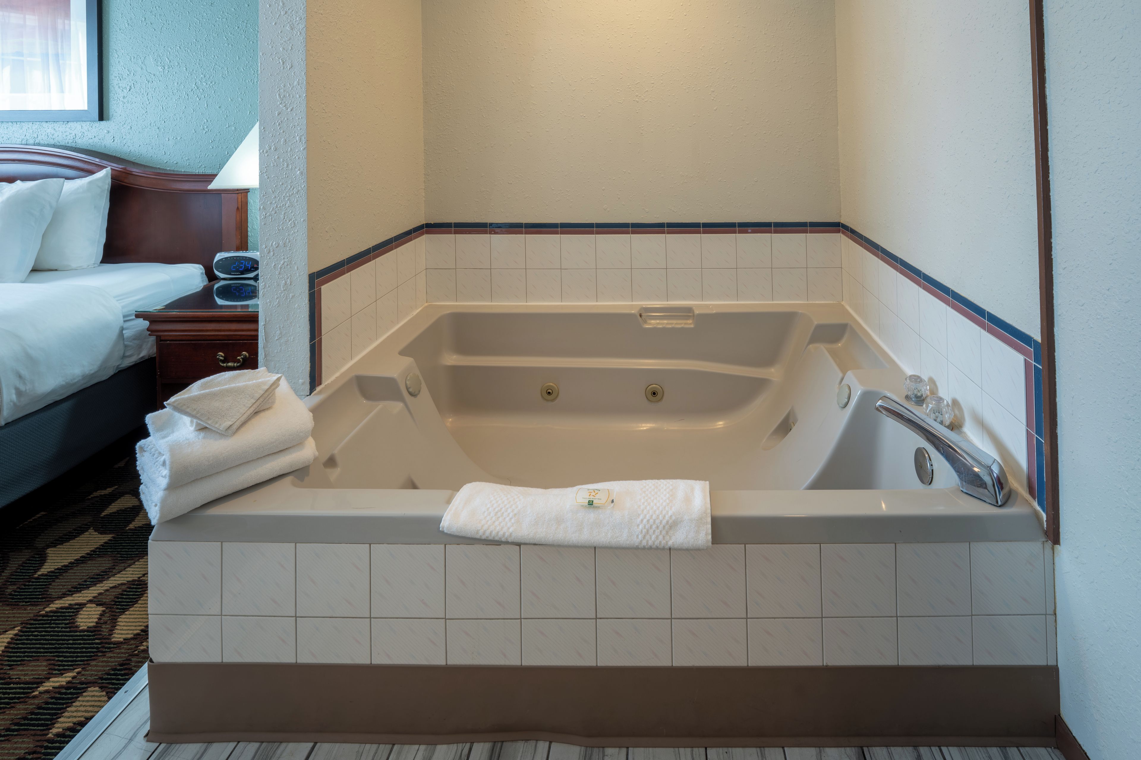 A hotel room with a large bathtub, a bed, and a bedside table.