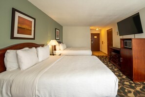 Une chambre d’hôtel avec deux lits, une télévision, un bureau avec une lampe et une moquette à motifs.