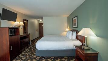 A hotel room with a bed, bedside lamps, a desk, a mirror, a television, and a patterned carpet.