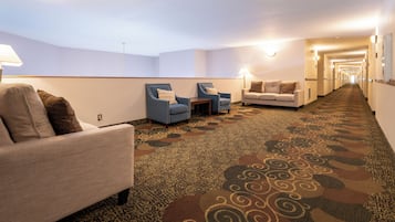 A hotel lobby with a carpeted floor, seating areas with armchairs and a sofa, and a long corridor leading to the exit.