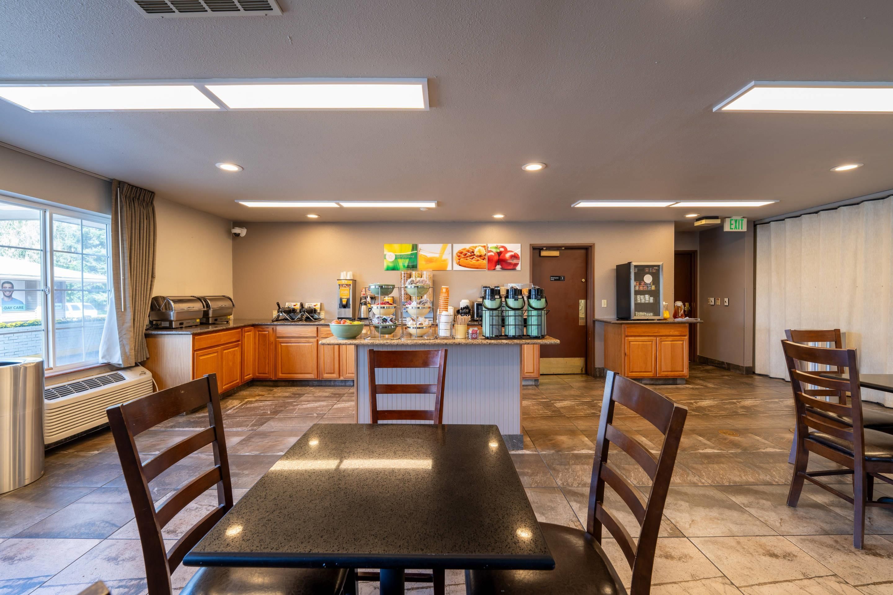 A spacious hotel kitchen with a central island, wooden chairs, and a dining table.