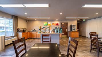 A spacious hotel kitchen with a central island, wooden chairs, and a dining table.