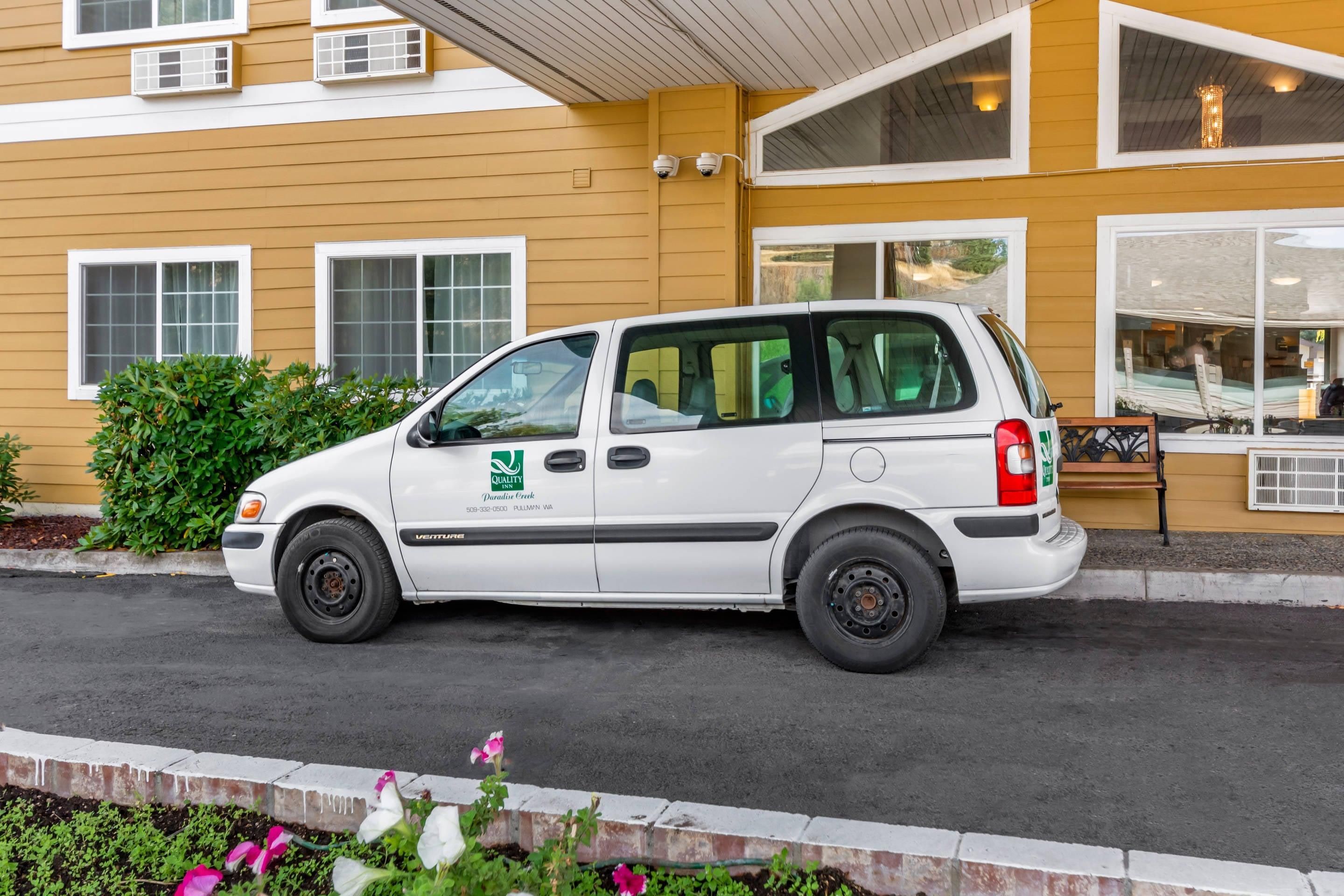 A white van parked in front of a yellow building with multiple windows and a visible awning.