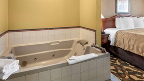 Una habitación de hotel con una bañera grande, una cama con ropa blanca y un cabecero de madera.