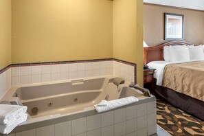 Una habitación de hotel con una bañera grande, una cama con ropa blanca y un cabecero de madera.