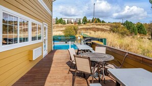 Una terraza de madera con mobiliario exterior, una piscina y vistas a una zona residencial.