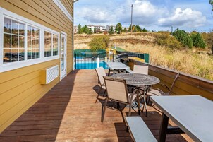 Una terraza de madera con mobiliario exterior, una piscina y vistas a una zona residencial.