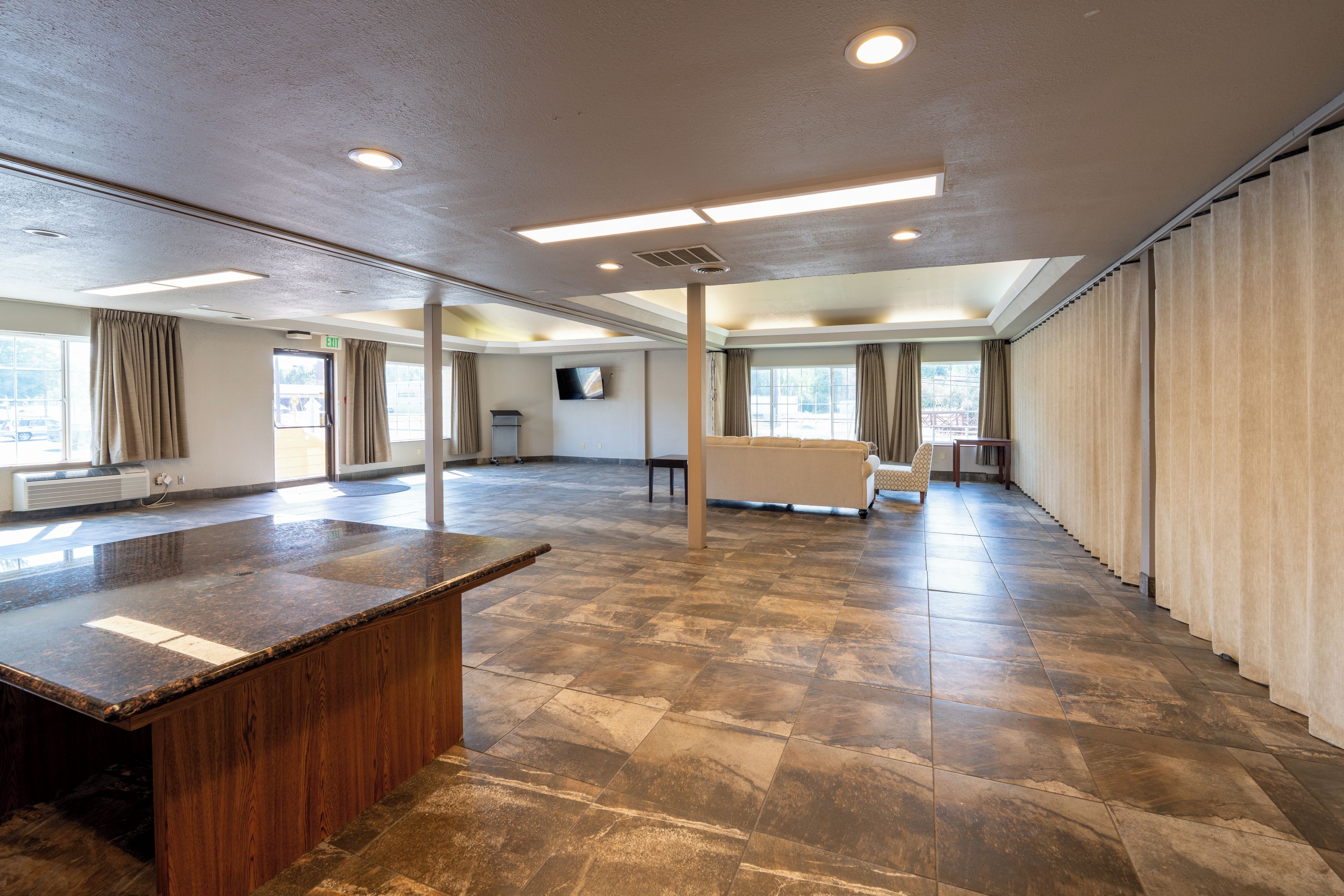 A spacious hotel lobby with a marble reception desk, large windows, and a flat-screen TV mounted on the wall.