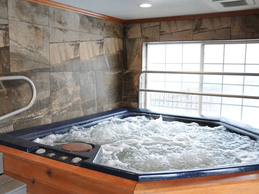 A hot tub with a wooden bench, stone walls, and a window with a view.