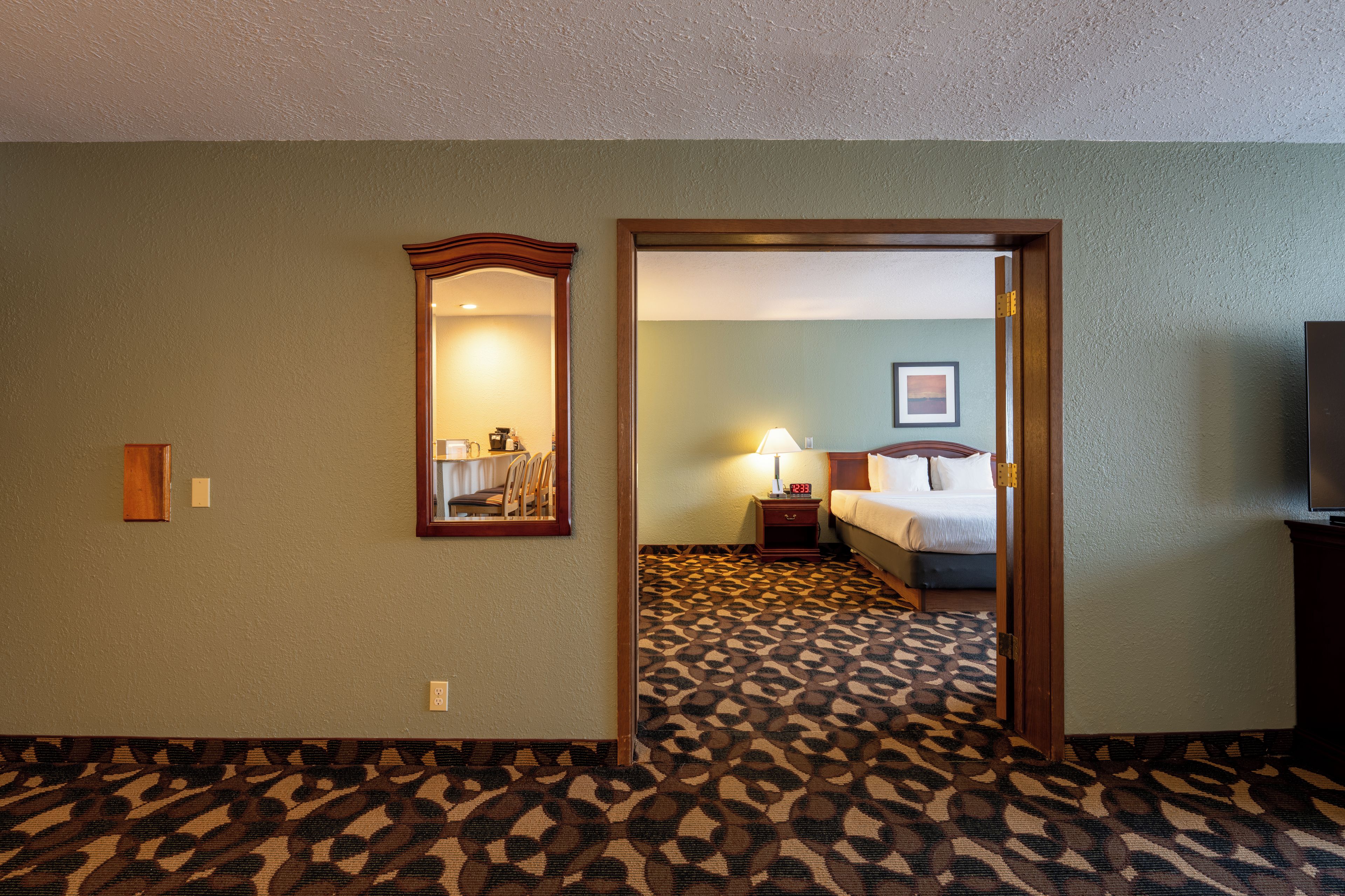 A hotel room with a bed, a nightstand, a lamp, and a mirror.