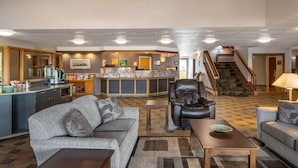 A hotel lobby with a reception desk, sofas, a coffee machine, and a staircase.