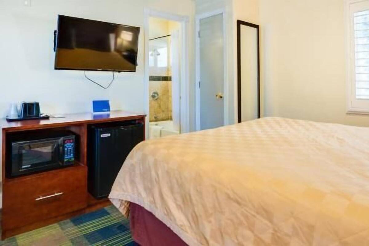 Habitación de hotel con cama, televisor montado en la pared, microondas y una pequeña mesa con cafetera.