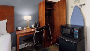 Habitación de hotel con cama, escritorio con lámpara, silla, microondas y armario.