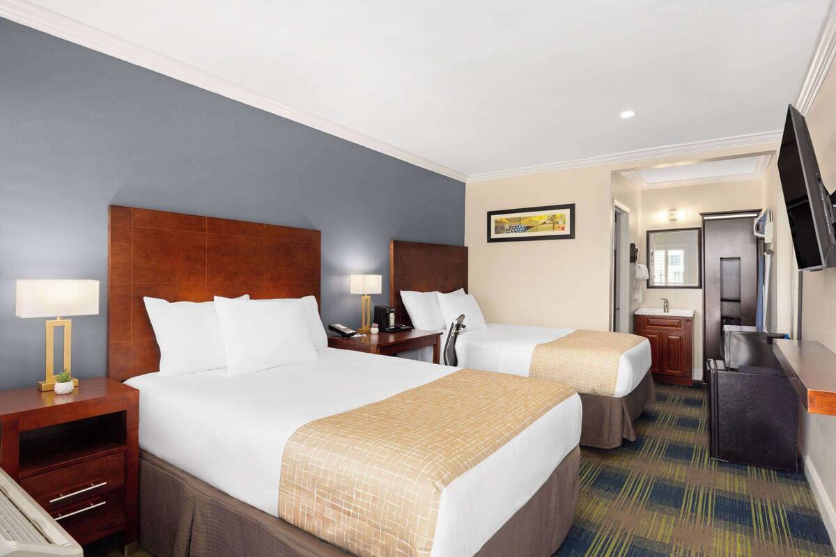 A hotel room with two beds, a desk, a TV, and a bathroom.