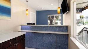 Zona de recepción con pared azul de azulejos, mostrador blanco y televisor montado.