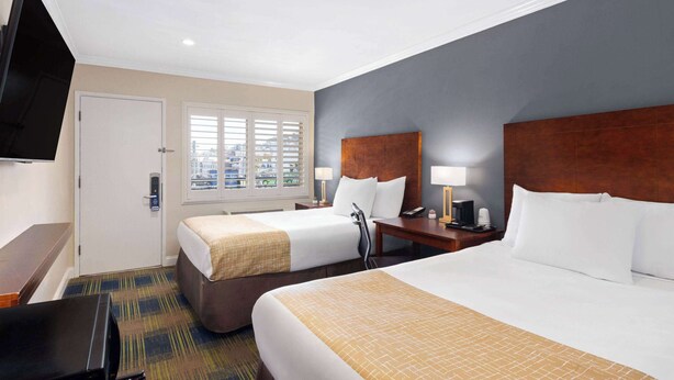 A hotel room with two beds, a television, a desk, and a window with blinds. - Travelodge by Wyndham by Fisherman's Wharf (San Francisco)
