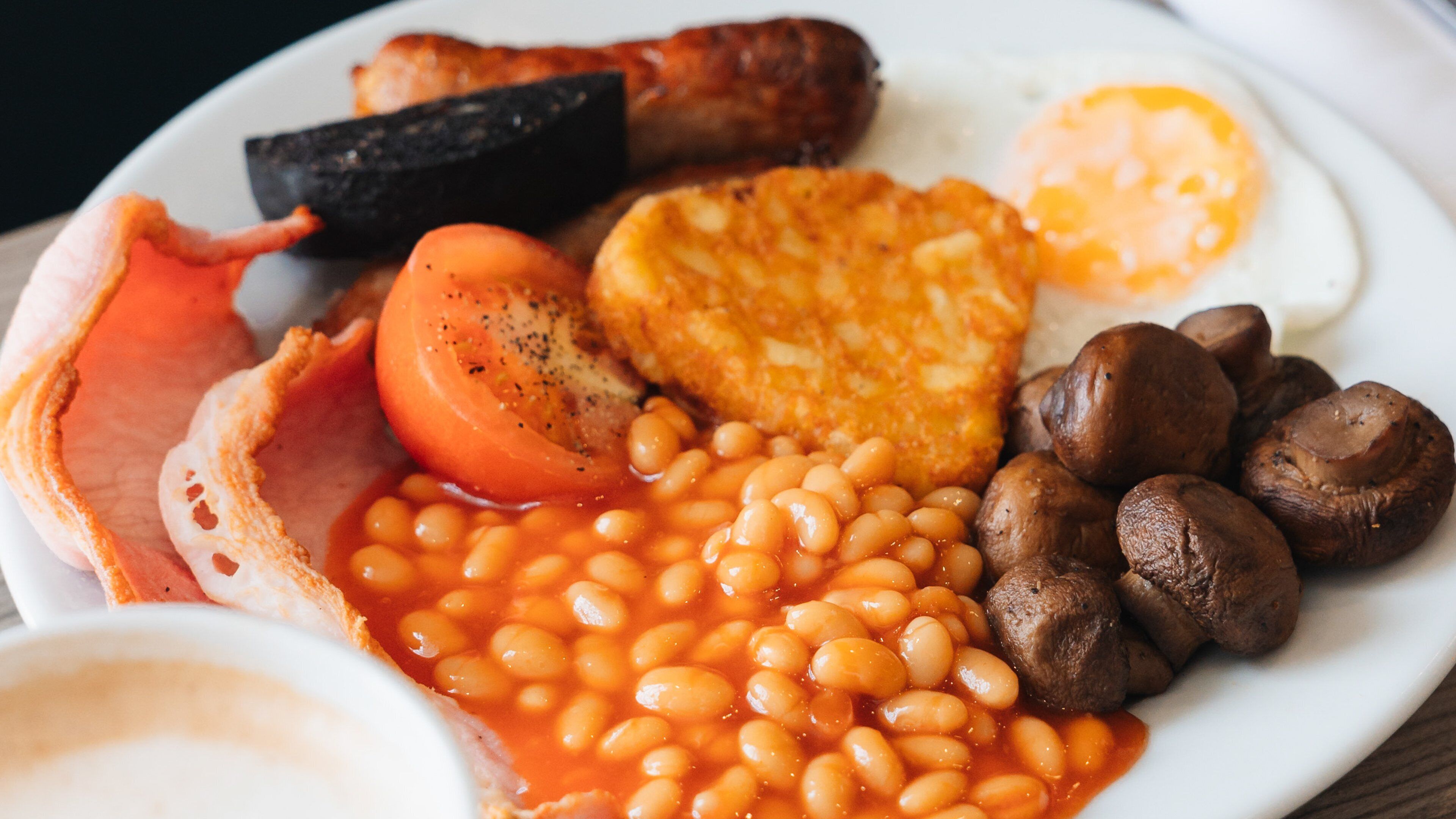 A plate of breakfast food including eggs, sausages, bacon, mushrooms, beans, and toast.