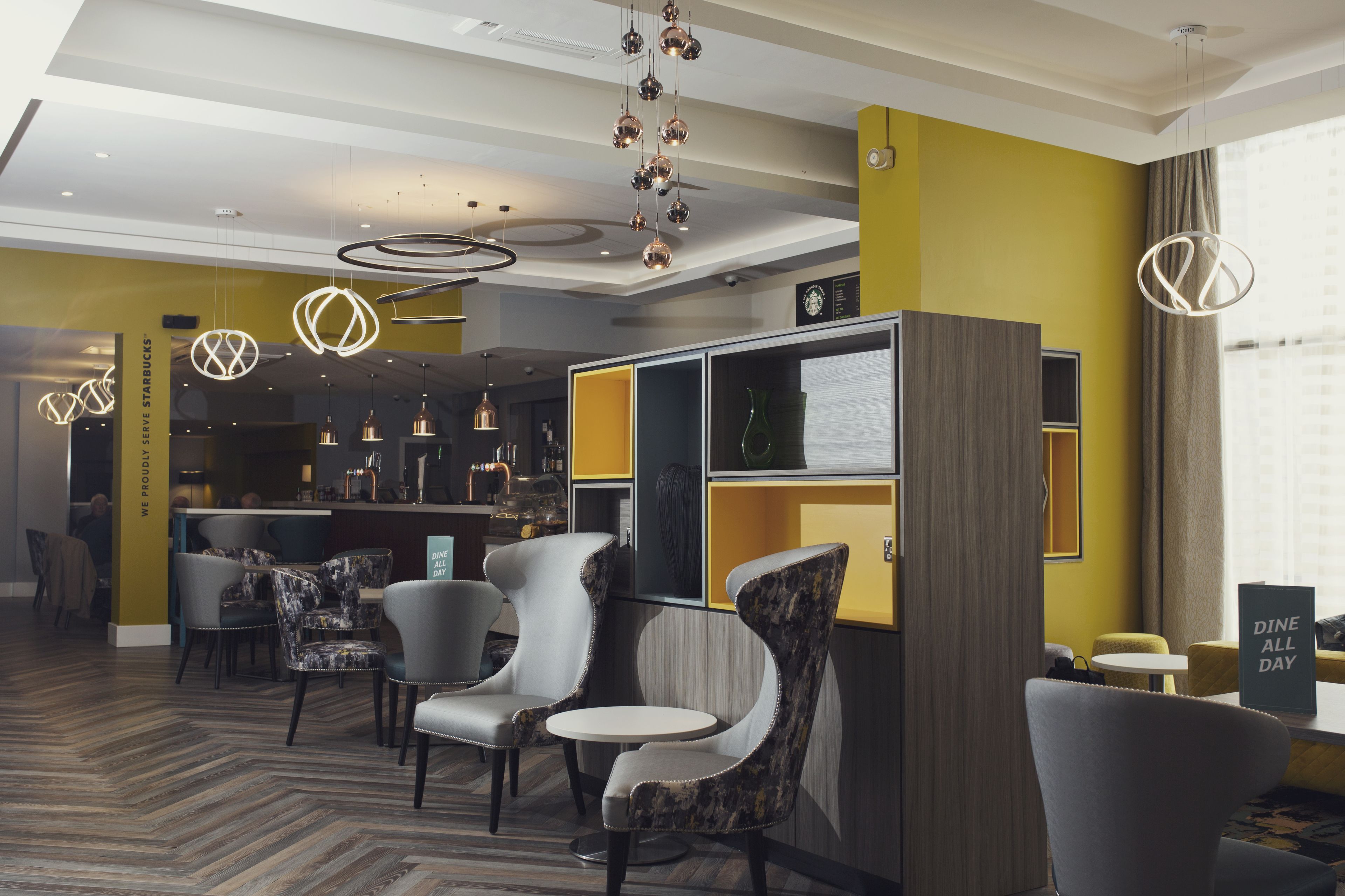 Un moderno vestíbulo de hotel con zona de bar, asientos y un letrero que dice 'Dine All Day'.