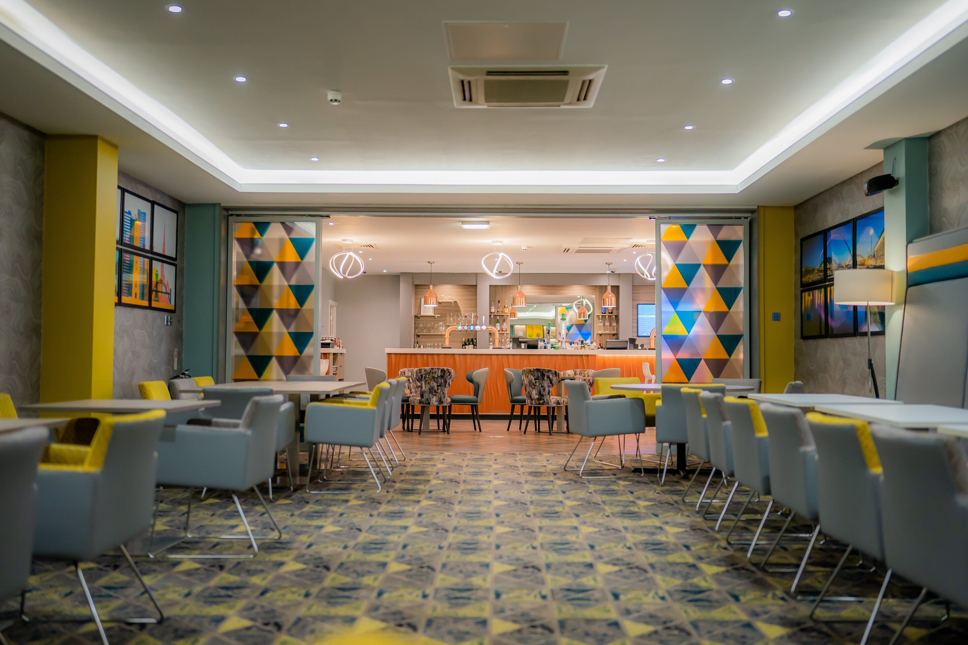 Un hall d’hôtel moderne avec un bar central, des espaces aménagés pour s’asseoir et un tapis à motifs.