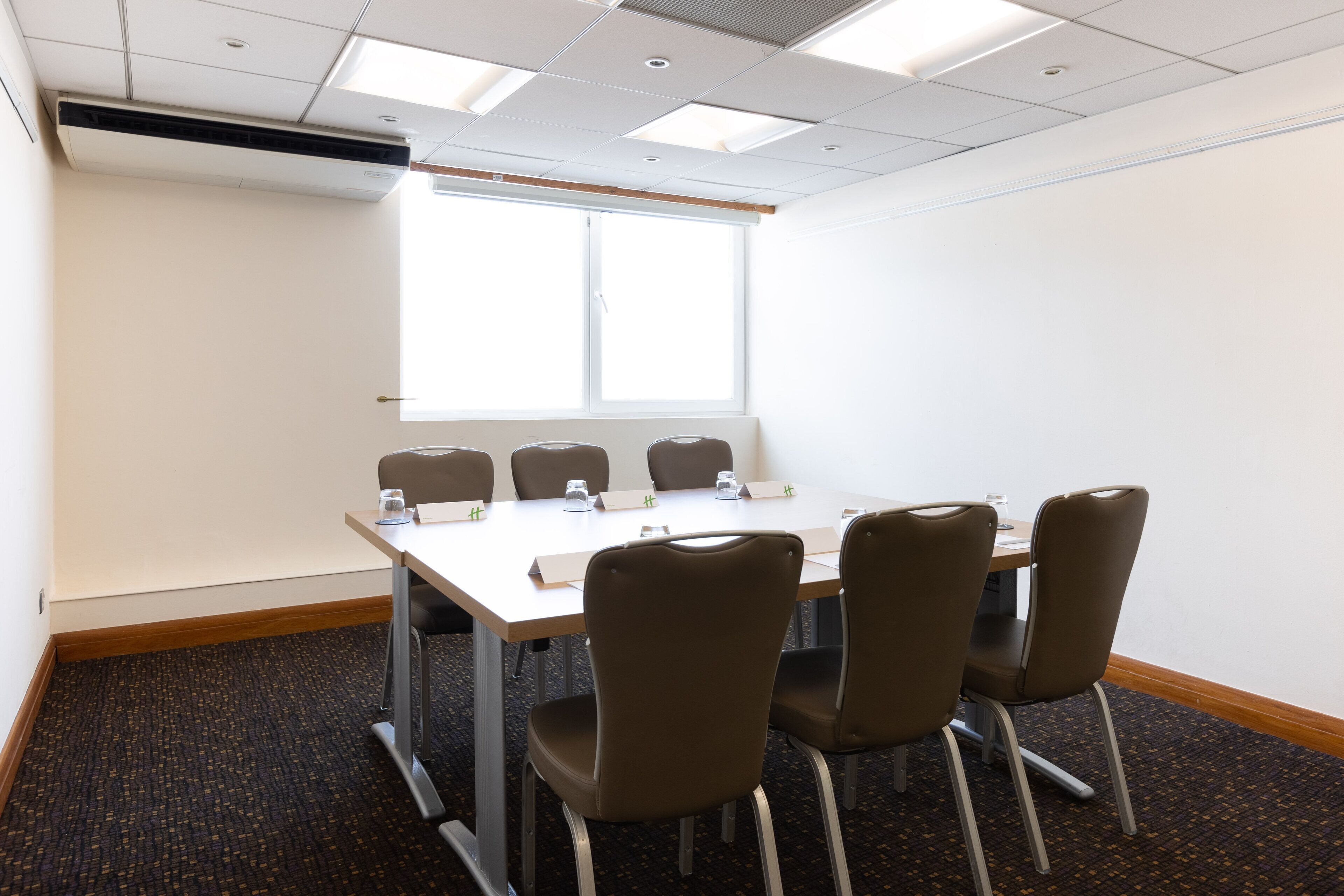 A conference room with a long table, six chairs, and a projector screen.