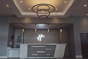 Un espace d’accueil au design moderne, comprenant un comptoir de réception, un grand panneau lumineux en forme de « H » et un plafond orné de luminaires circulaires.