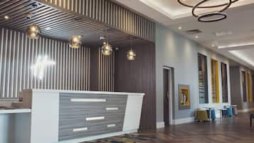 Een moderne receptie met een plafond van houten latten, een receptiebalie en een zithoek met blauwe stoelen.