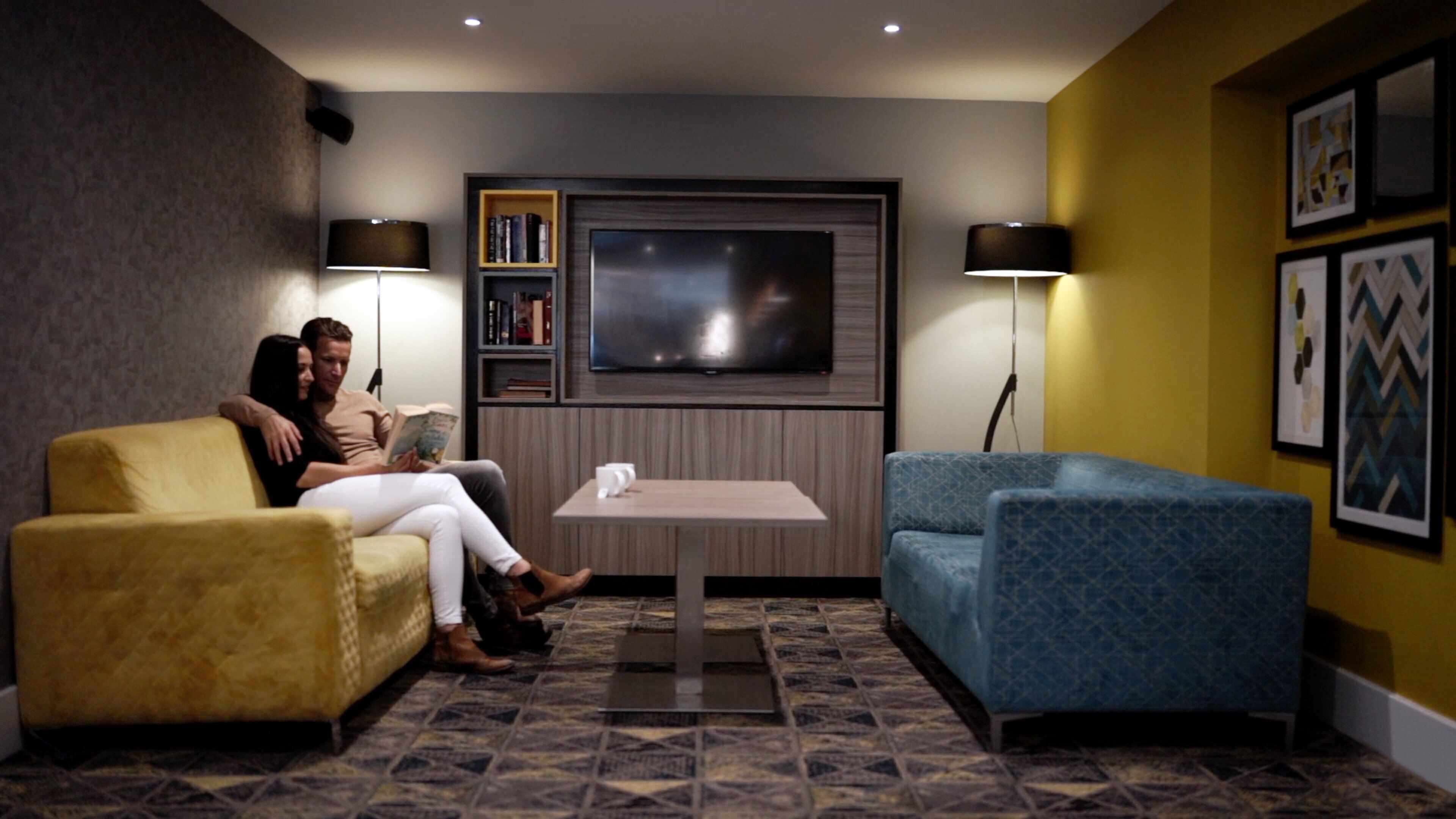 A cozy living room with a sofa, a blue armchair, a small table, and a bookshelf.