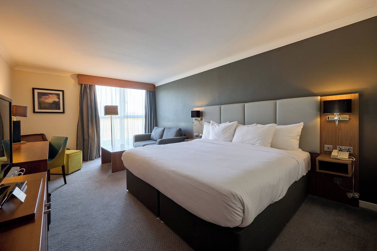 A hotel room with a large bed, a desk with a computer, a chair, and a small table.
