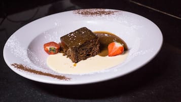 A dessert plate with a square piece of cake, a strawberry, and a dollop of cream.